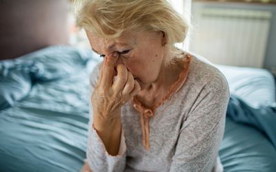 An older person feeling sinus pain sitting on a bed at home