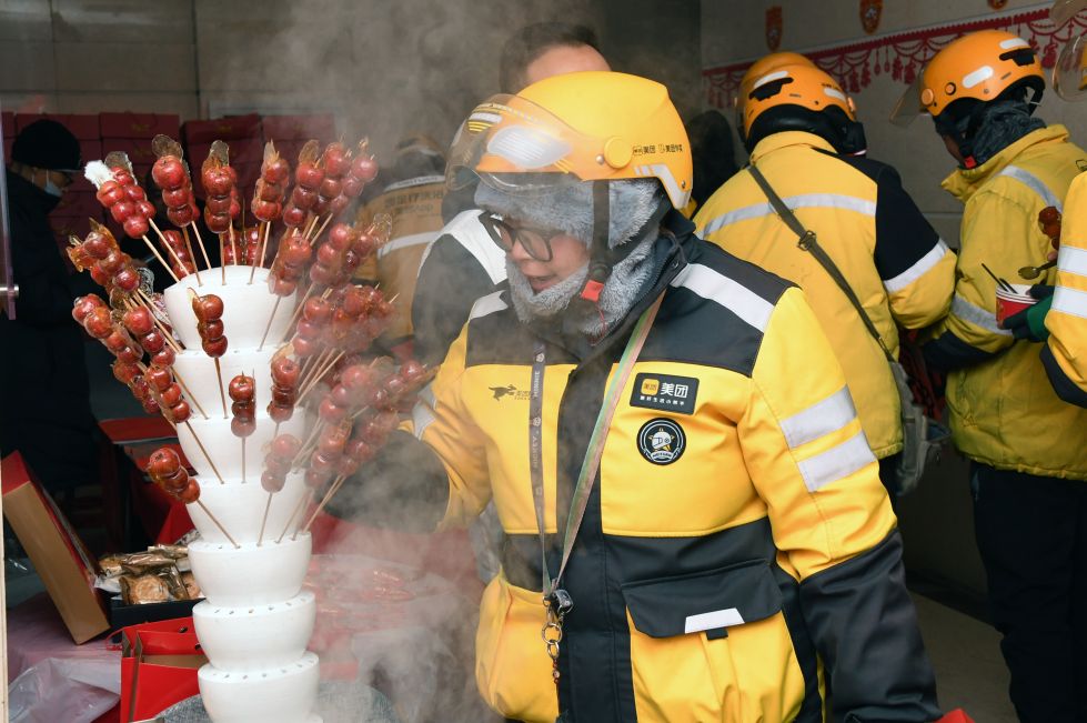 2024年 1月23日，在北京市海淀区北太平庄街道户外劳动者暖心驿站，一名外卖员（前）准备品尝糖葫芦。 新华社记者 任超 摄
