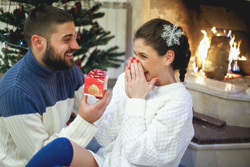 在圣诞节装饰的房子内部，一对恩爱的夫妇靠近壁炉。女朋友收到了他男朋友送的圣诞礼物图片下载
