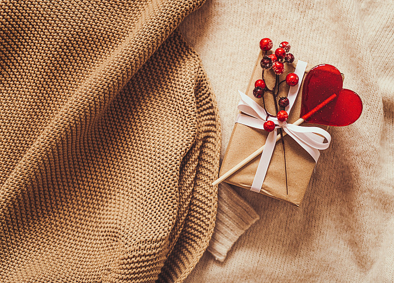 圣诞节和寒假平铺背景与包装的圣诞礼物和红心棒棒糖在棕色毛衣的背景图片下载