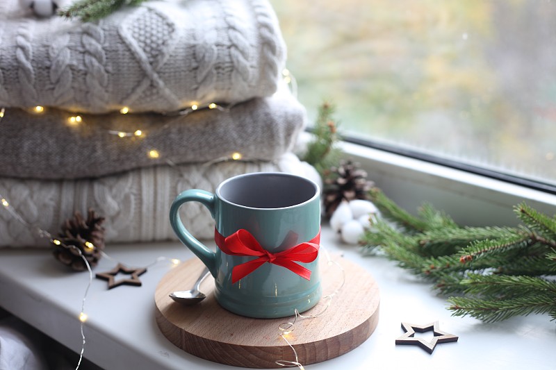 温馨的家庭图片的蓝色陶瓷杯与咖啡在窗台上，圣诞装饰，温暖的针织毛衣和松树绿色的树枝在背景图片下载