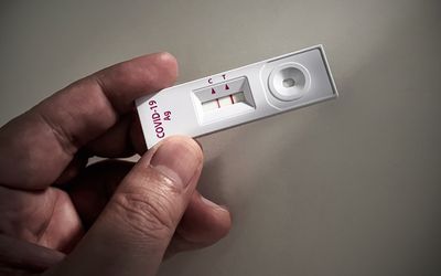 A person's hand holding a positive COVID-19 test
